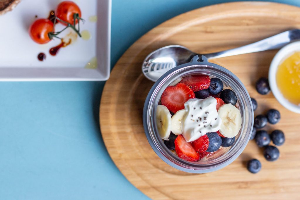 tabletop view of a breakfast with yogurt, fresh berries and banana slices, on a wooden plate.
