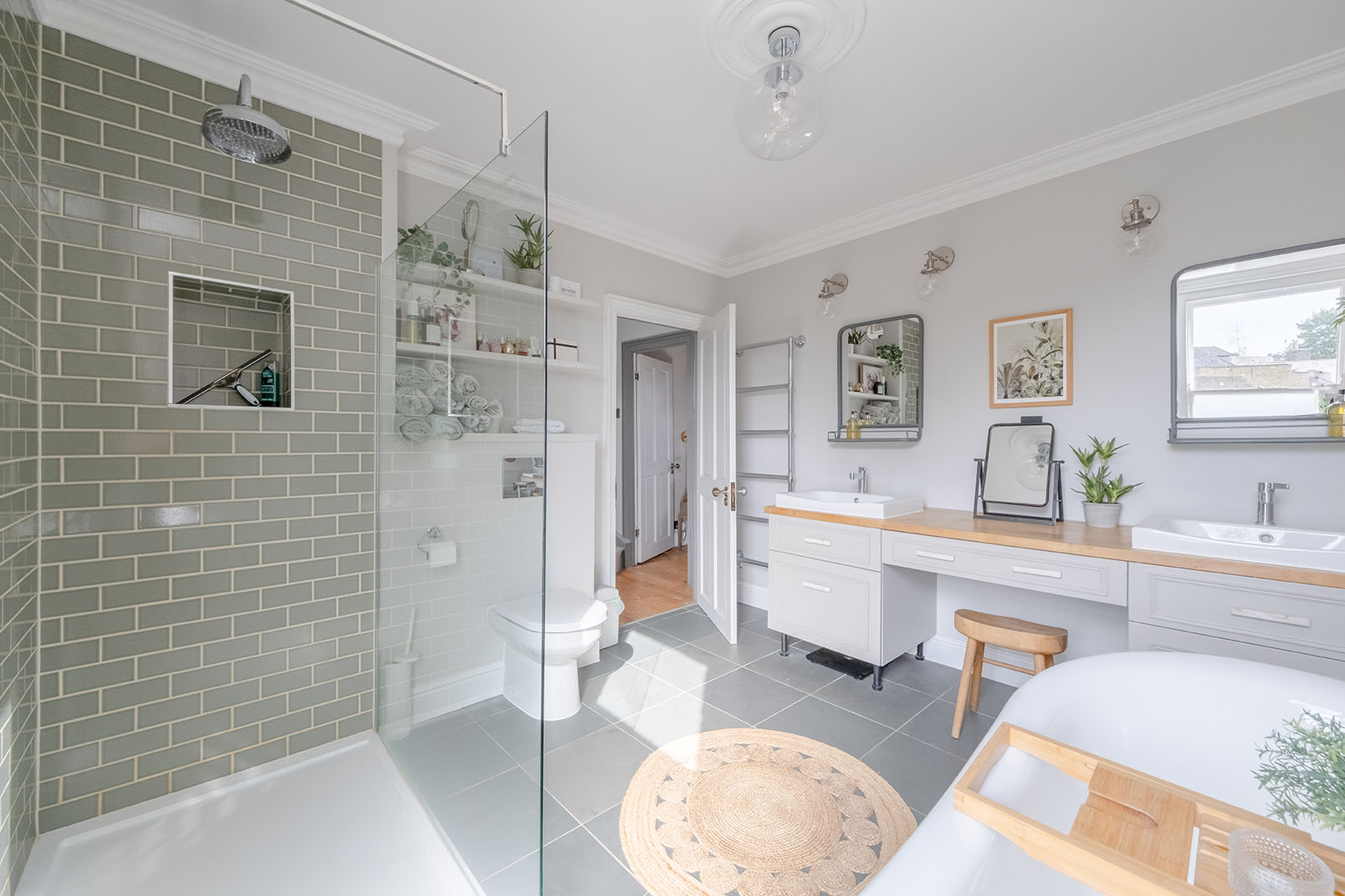 a bathroom photo from a property photography series, natural colours, bright and modern design space, light grey walls, double sink counter with light green details, looking towards the entrance of the space, showing partially the shower screen