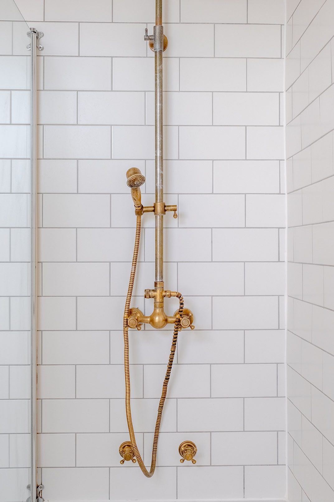 A shower detail property photo with a gold bronze coloured shower head and white wall tiles.