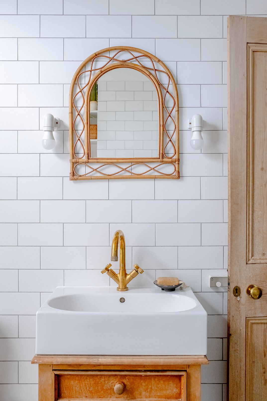 A detail of a bathroom mirror and sanity unit, white tiles on the wall, bronze gold coloured tap.