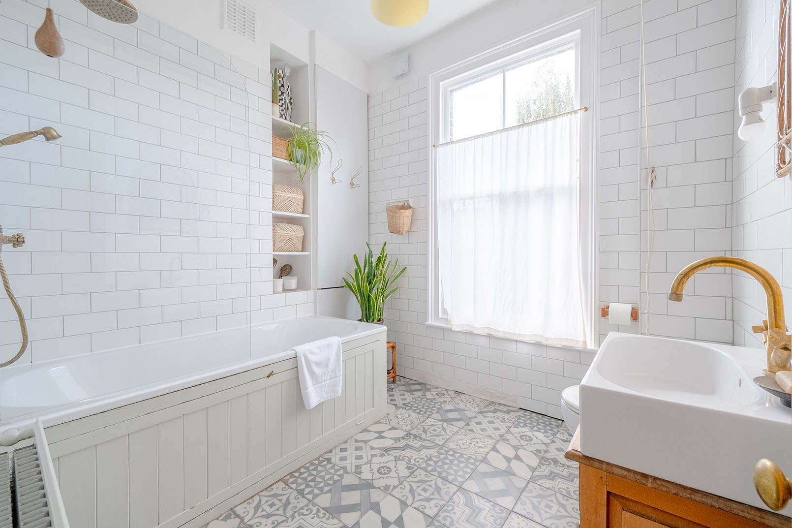 A large bathroom with white tiles, grey patterned floor tiles and a large window taking lots of daylight inside, taken for property photography.