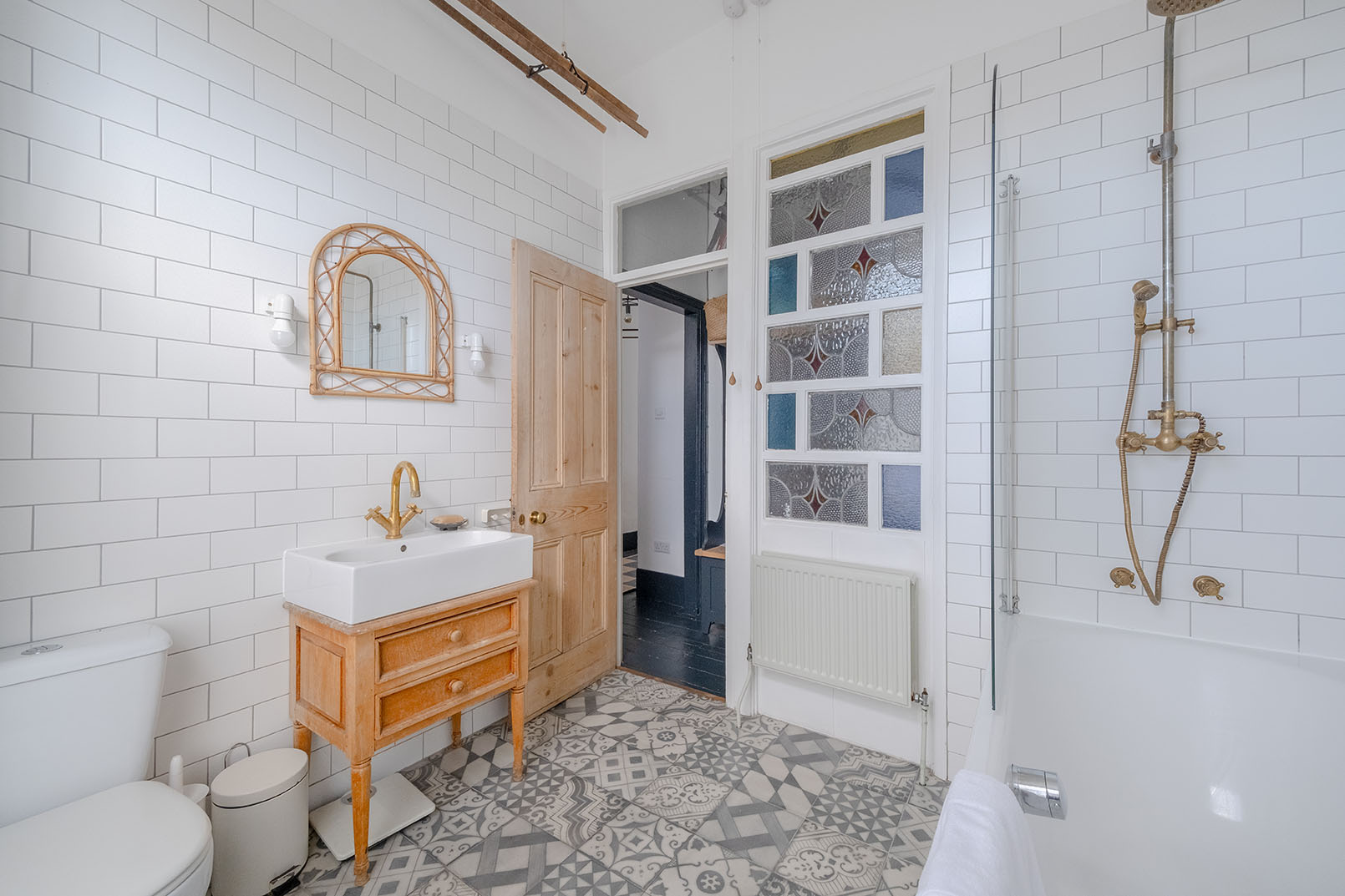 A large bathroom with white tiles, wooden vanity cupboard and grey patterned floor tiles taken for property photography.