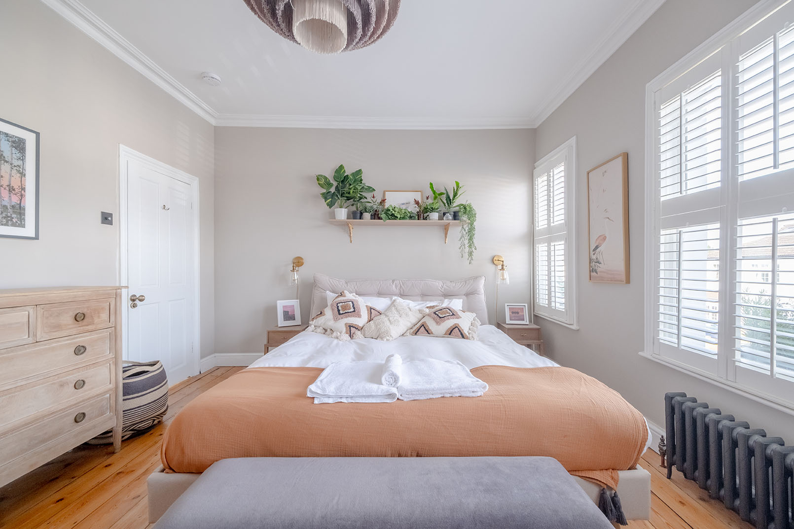 a bedroom, bright and well decorated, photo taken directly from the front of the bed, still capturing the whole room for property photography.