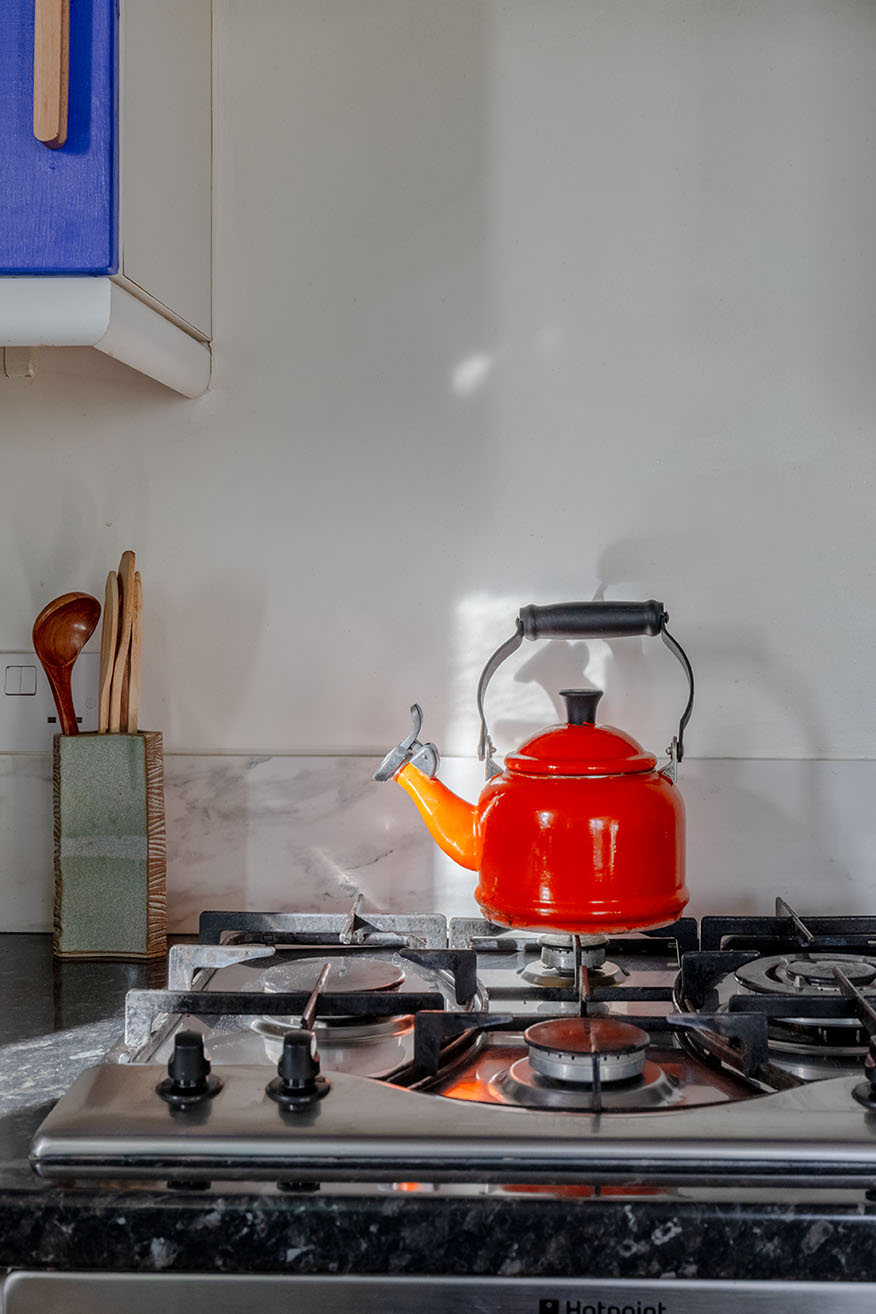 An Airbnb detail property photo of a kitchen, a gas hob and a red kettle on the stove.