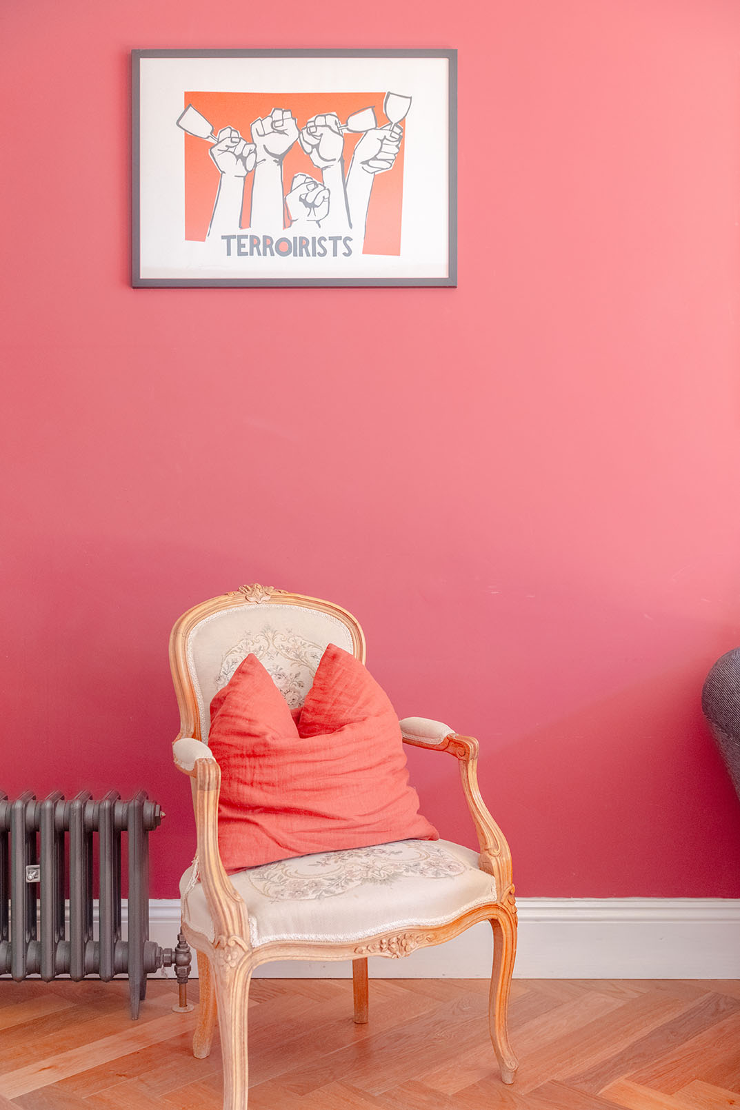 A bright, candy pink coloured wall, an armchair with beige upholstery and wooden arm in front of the wall, airbnb holiday letting property photography.
