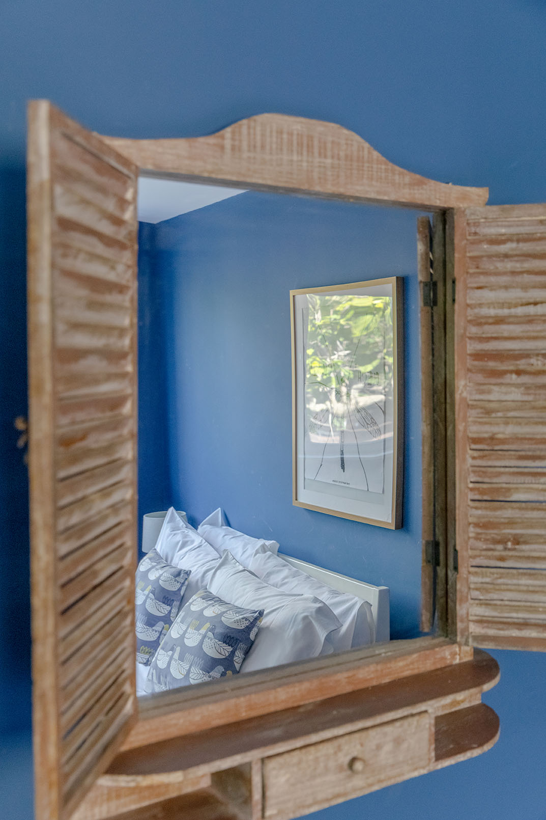 A nice blue painted wall and a small mirror on it, the reflection of a bed, detail property photography for a holiday property listing.