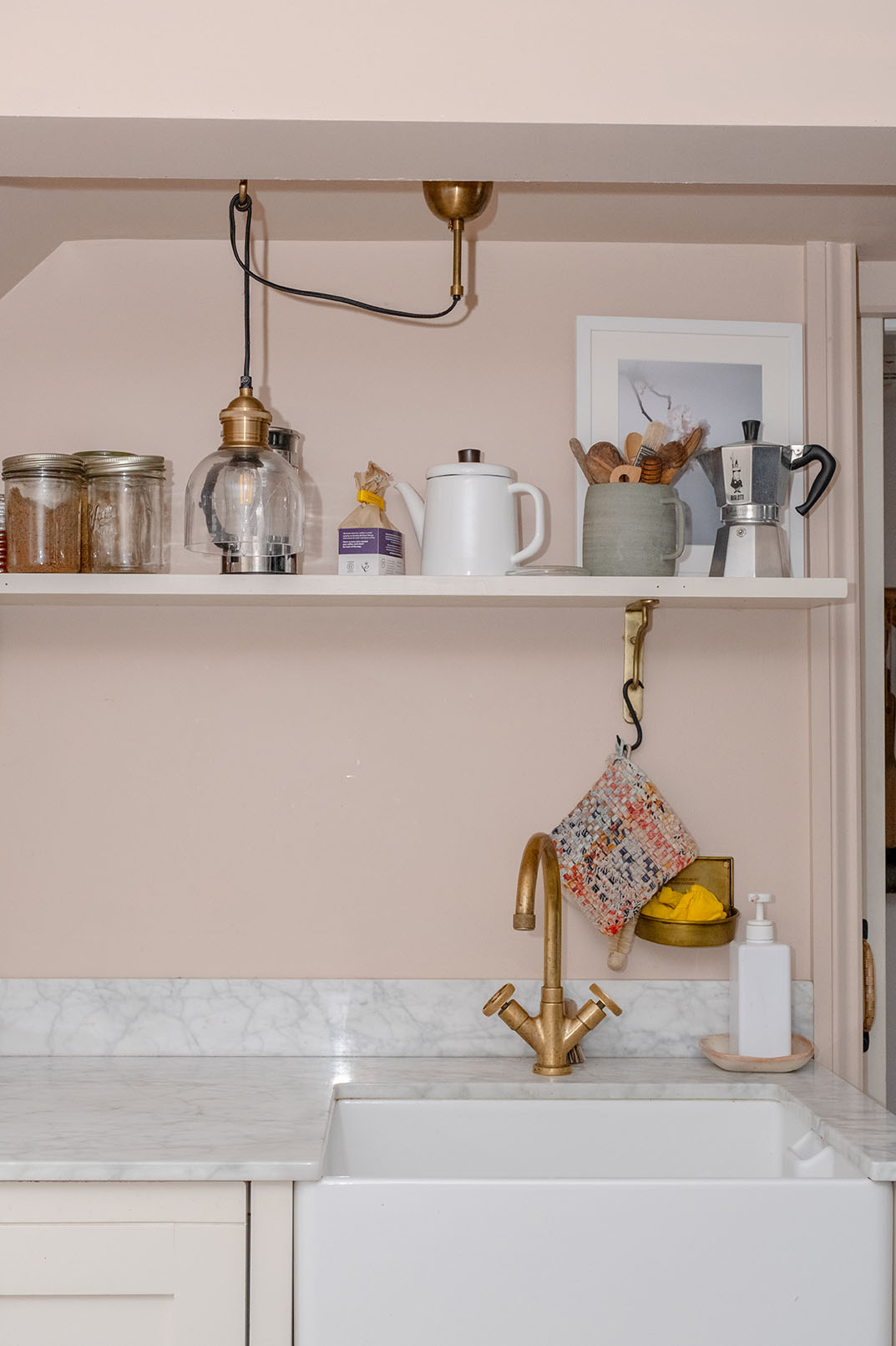 Close up shot of a kitchen sink area with a shelf on the wall and some kitchen items on it, taken for property photography to be used on holiday letting listing.