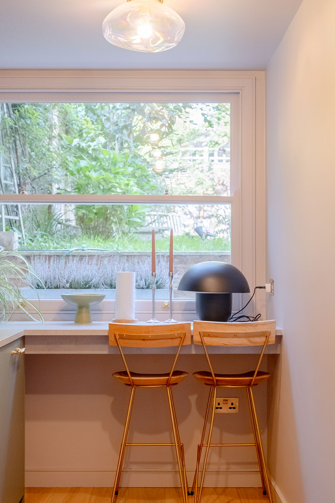 A kitchen detail photograph captured for sales property photography, giving the vibe of the area with high stools in front of a large window looking to a green area.