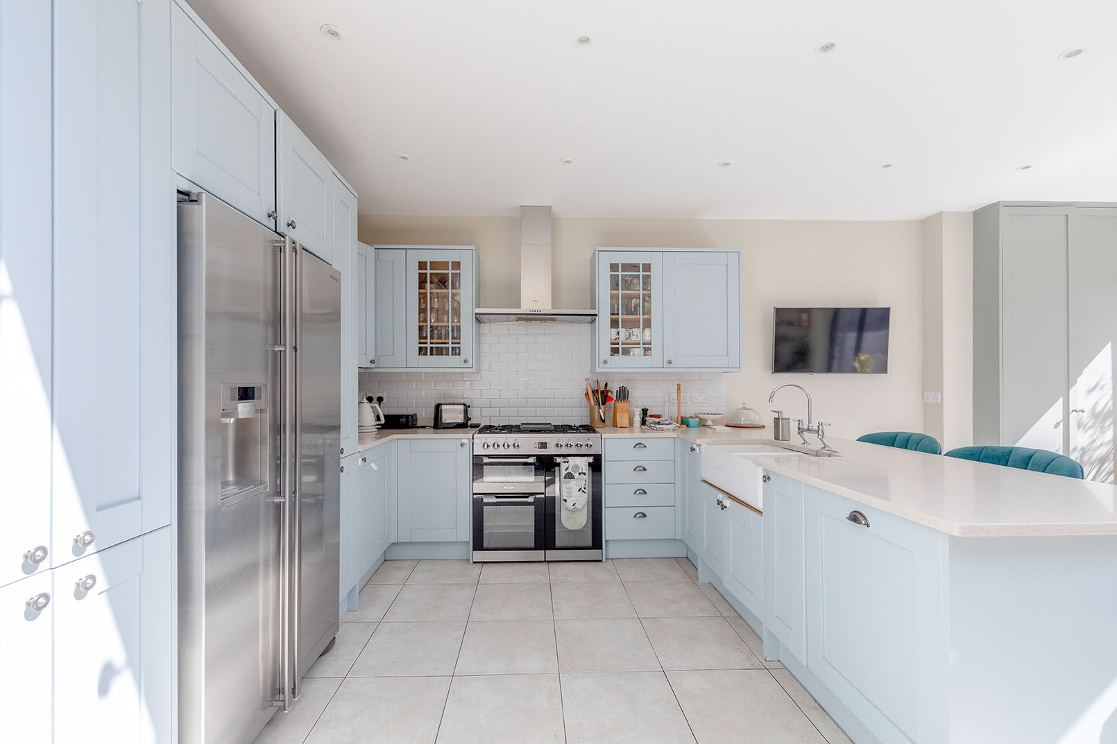 Direct angle of a large, open plan kitchen with light blue cupboards, modern design and showing all the appliances.