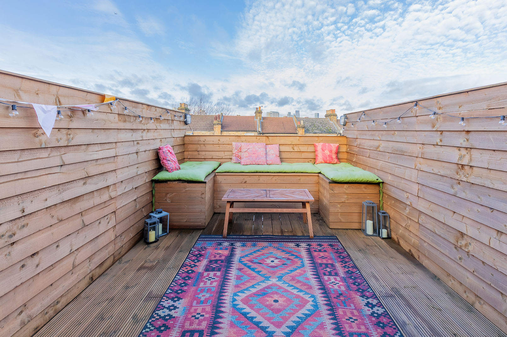 a wood floor and paneled terrace with a colourful seating and a colourful rug, taken for an airbnb listing