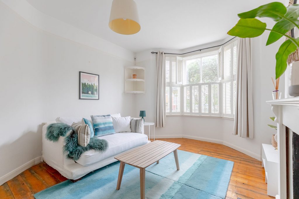 Direct angle for property photography of a Image of a smaller living room with wooden floor, a light blue coloured carpet on the floor, white walls and a large window captured for property photography.