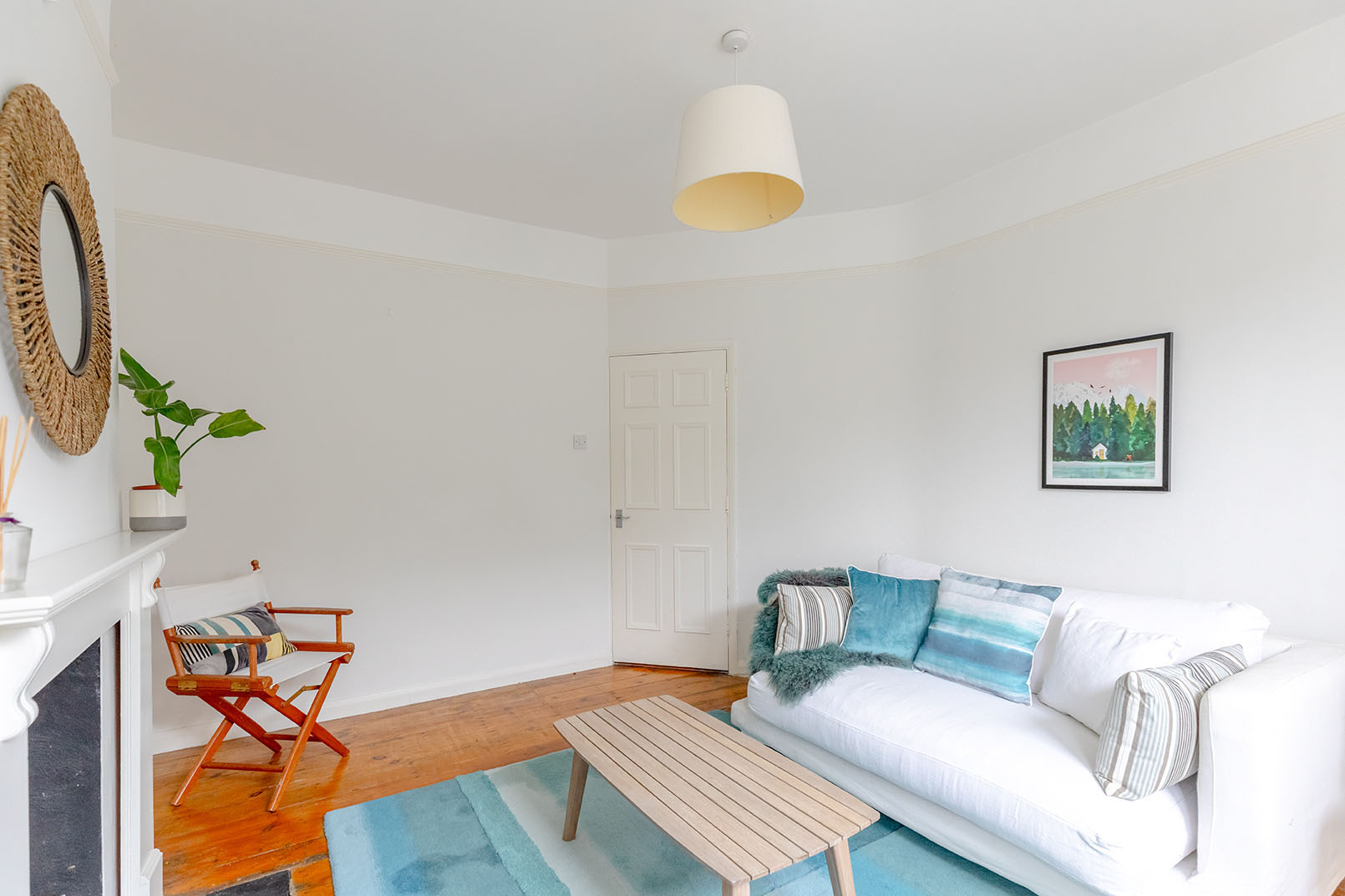 Direct angle for property photography of a Image of a smaller living room with wooden floor, a light blue coloured carpet on the floor, white walls and a white sofa with blue cushions.