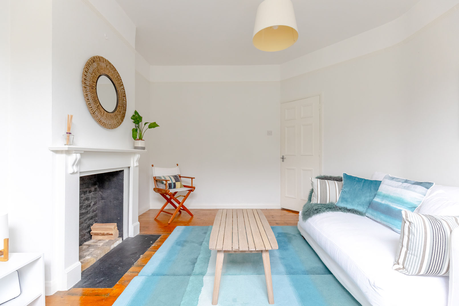 Direct angle for property photography of a Image of a smaller living room with wooden floor, a light blue coloured carpet on the floor, white walls and a fireplace.