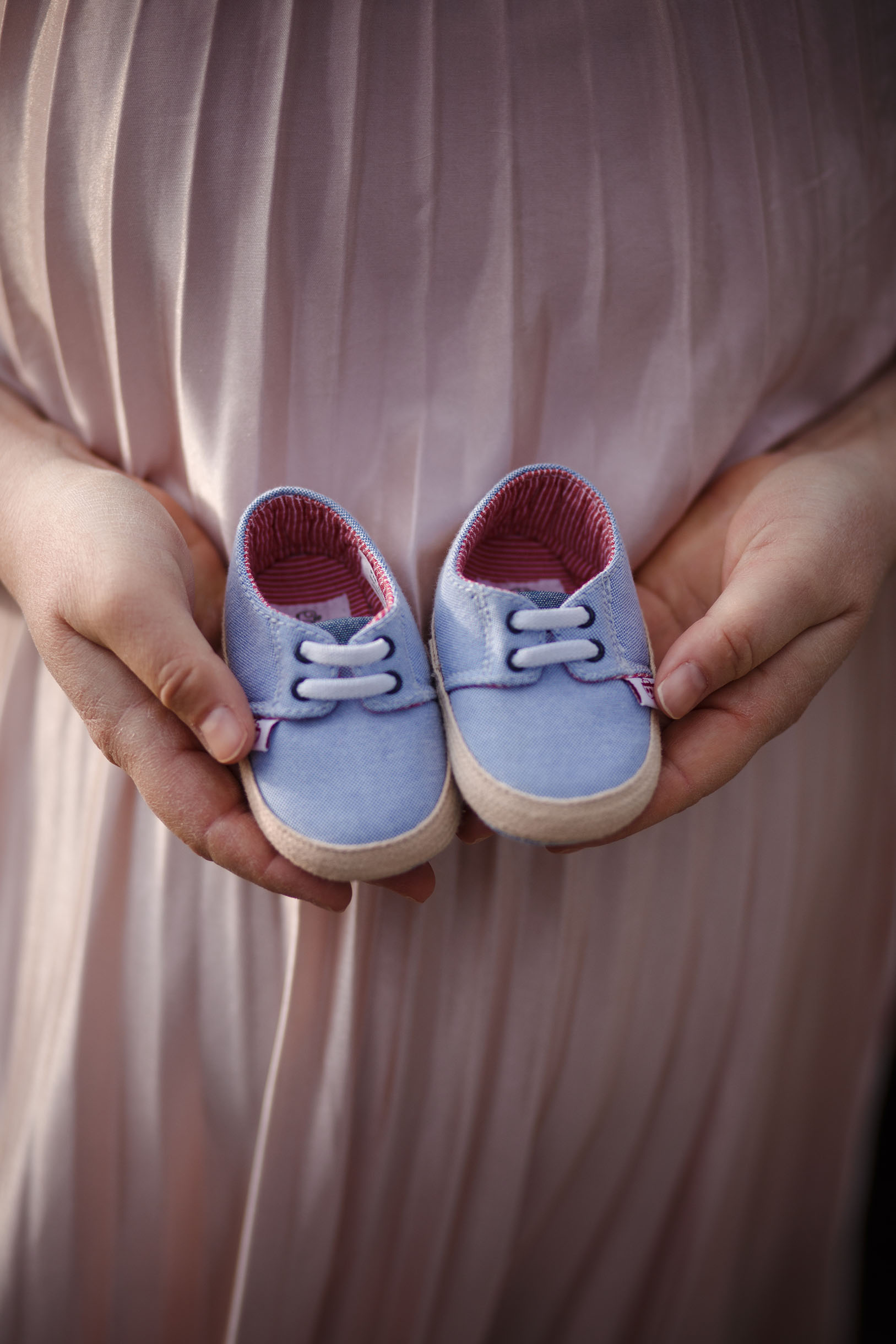 Pregnant woman holding her baby's shoes in her hands, close up shot for family photography.