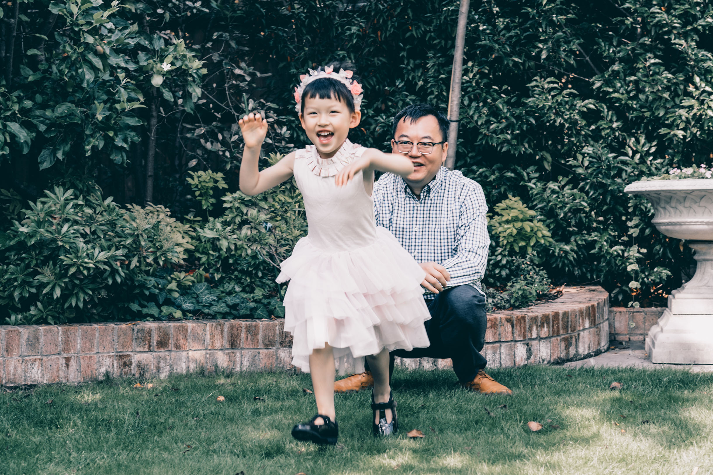 Father looking after her daughter, running in their garden, enjoying the day while being captured for family portrait photography.