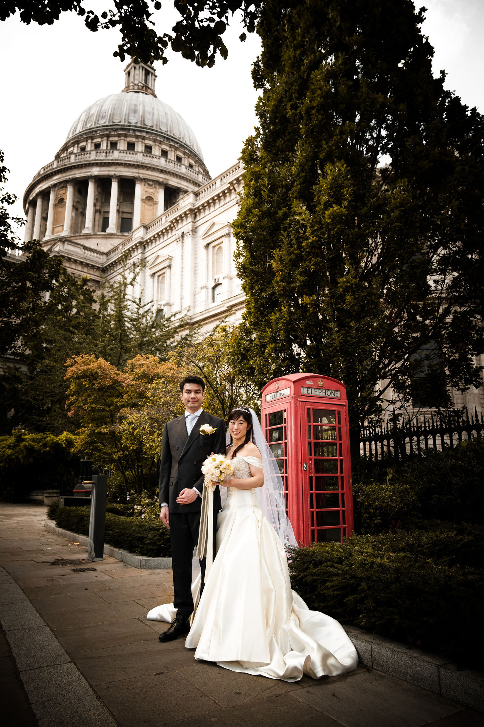 An image of a newly wed couple in front of a classic British red phone booth, St Paul's cathedral is seen on the background.