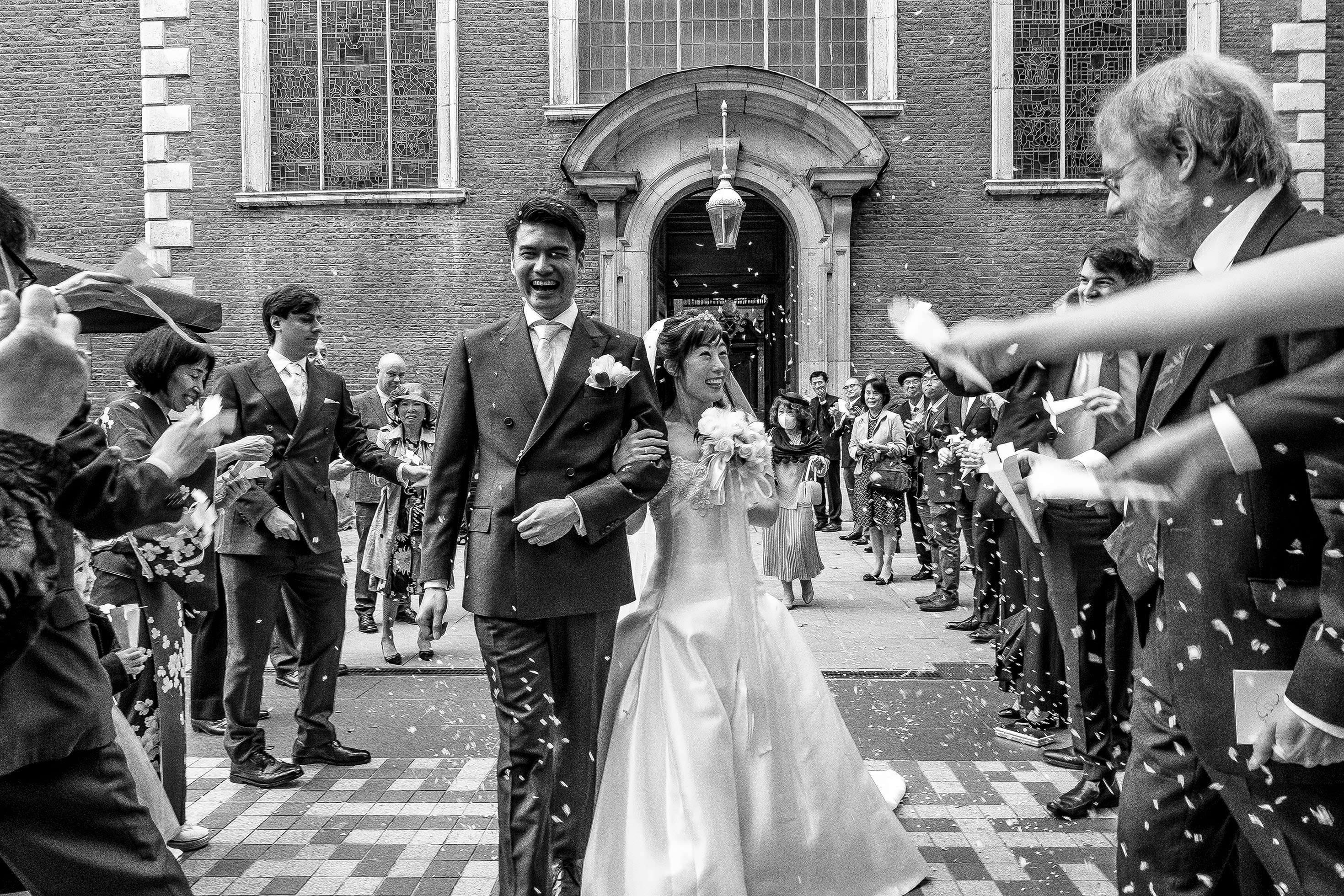 black and white wedding photo, couple coming out of church and walking amongst their loved ones.
