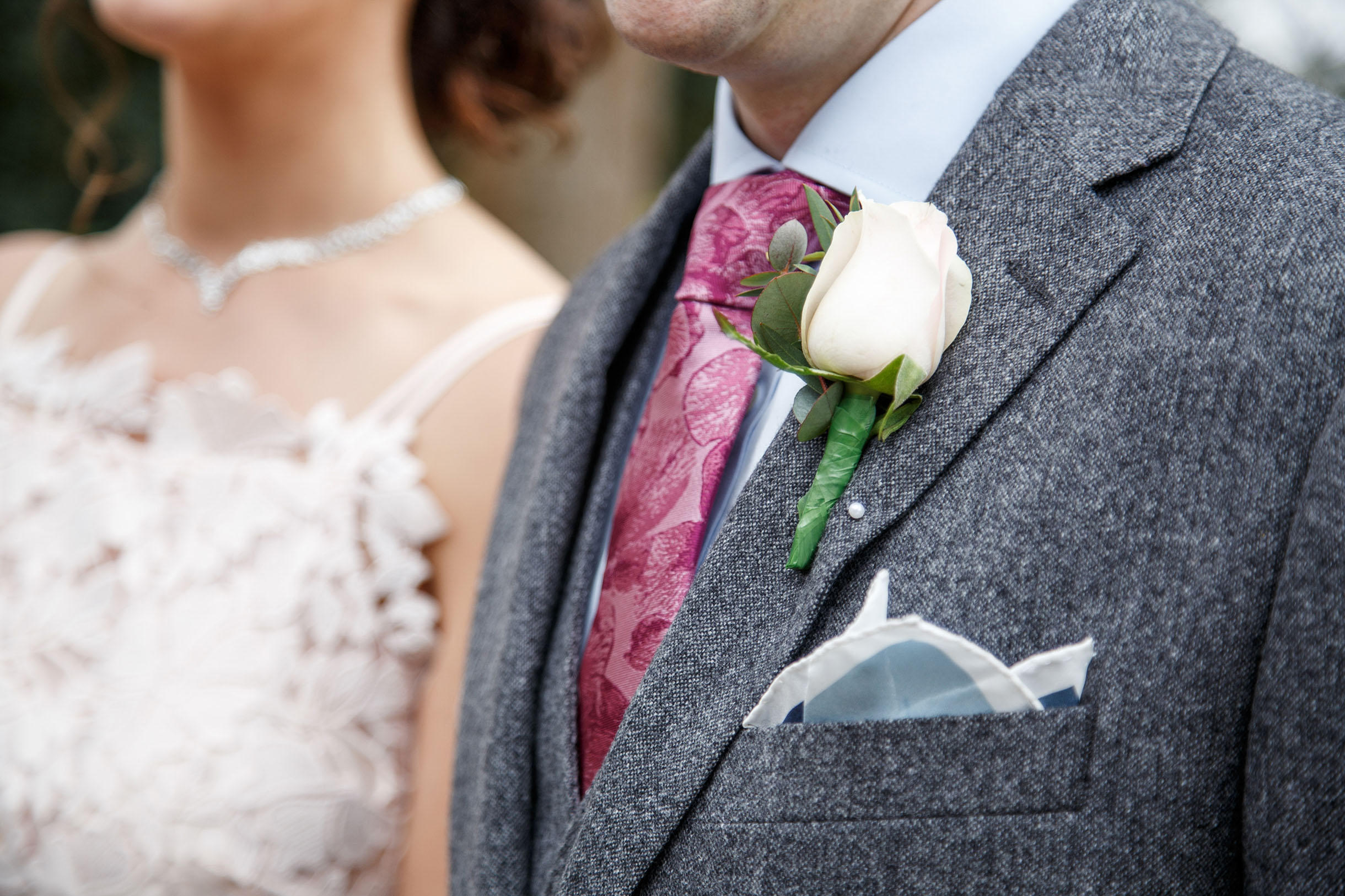 Close up shot of a couple, focusing on groom's chest with a flower attached to his jacket.