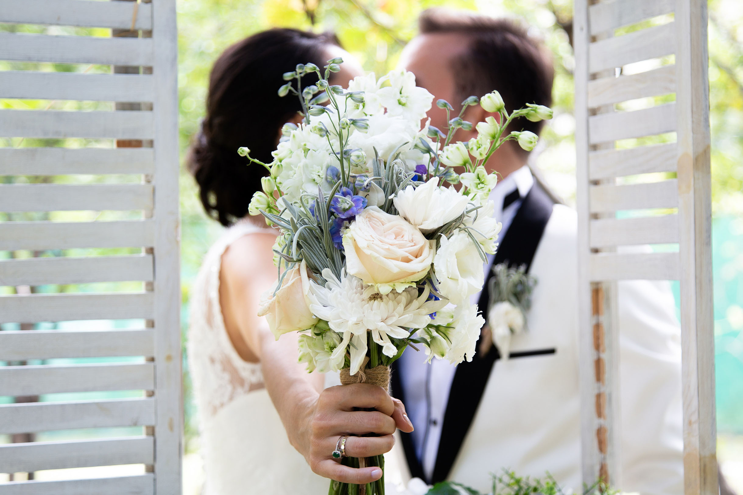 a couple kissing and posing, bride extending the bouquet to the camera, hiding their faces.