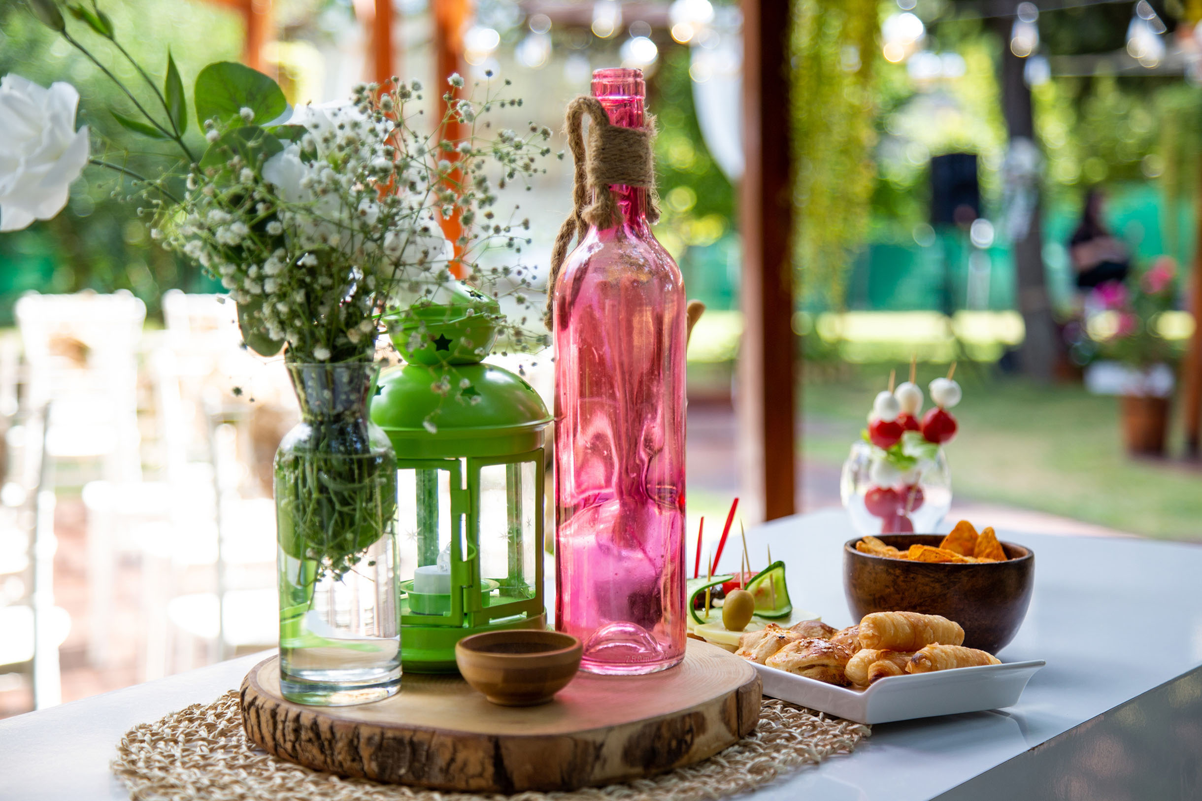 Detail image from a wedding with coloured glass bottles and a lantern on a wooden plate at an outdoor space.